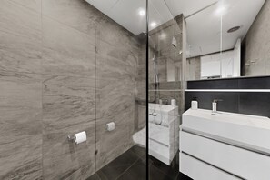 Un baño moderno con cabina de ducha de vidrio, un lavamanos blanco y una pared de mármol.