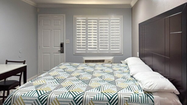 A bedroom with a bed, a window with blinds, a door, and a small table. - 1 King Bed|Non-Smoking, Micfridge (Oakland)