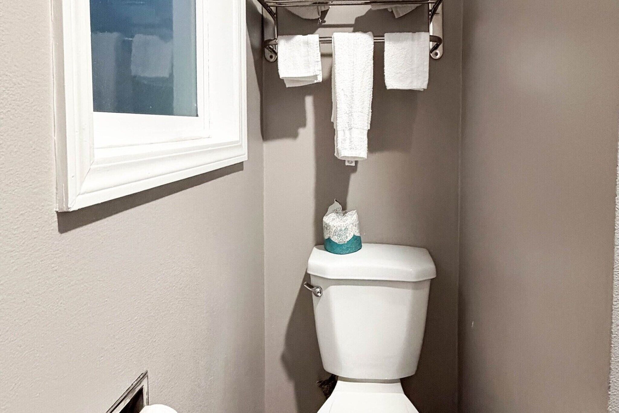 Un baño con inodoro, perchero para toallas y una ventana.