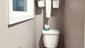 Un baño con inodoro, perchero para toallas y una ventana.