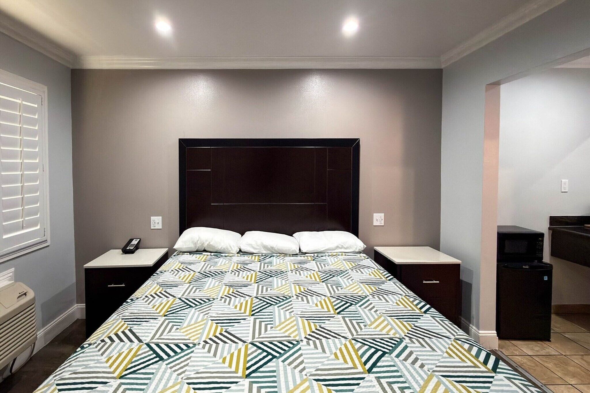 A bedroom with a bed, nightstands, a telephone, a microwave, and a trash bin.