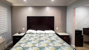 A bedroom with a bed, nightstands, a telephone, a microwave, and a trash bin.