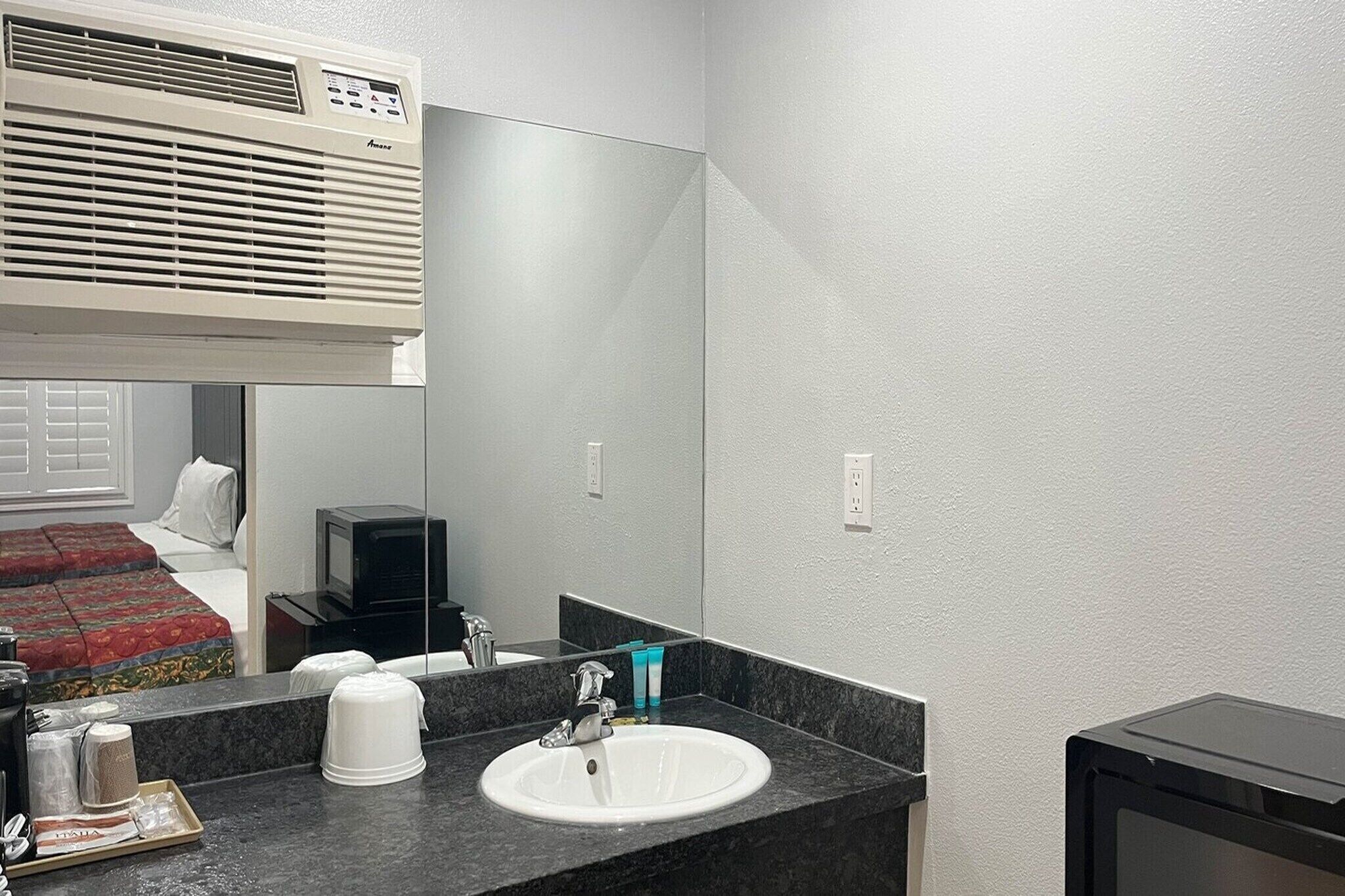 A hotel bathroom with a white sink, mirror, and a ceiling-mounted air conditioner.