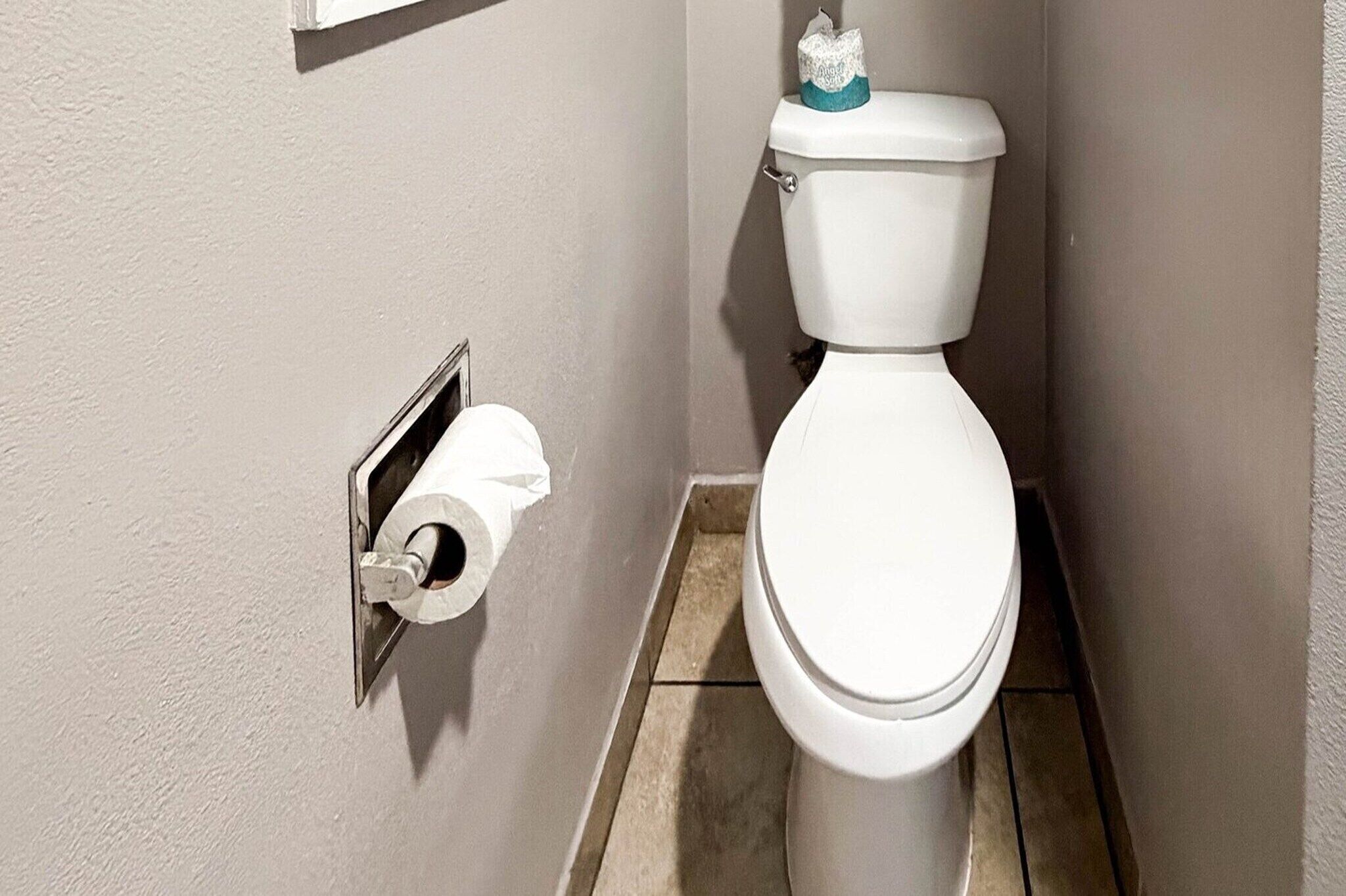 A toilet with a paper towel holder and a toilet paper roll mounted on the wall.