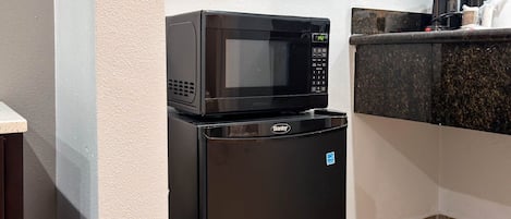 A compact kitchen with a microwave and refrigerator, a countertop with a coffee maker, and a tiled floor.