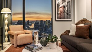 A modern living room with a city view, a sofa, a chair, a lamp, and a framed picture on the wall.