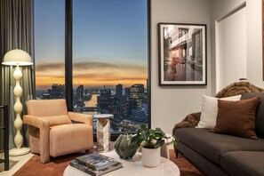 Ein modernes Wohnzimmer mit Blick auf die Stadt, inklusive Sofa, Sessel, Lampe und einem gerahmten Bild an der Wand.