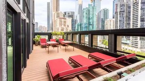 A rooftop terrace with lounge chairs, a table, and potted plants.