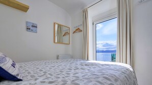 Un dormitorio con cama, ventana con cortinas, calentador en la pared y vista al mar.