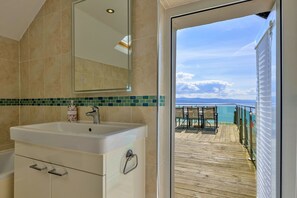 A bathroom with a large mirror, a sink, and a view of a wooden deck and ocean. - Finest Retreats | Awel Y Mor (Criccieth)