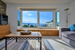 A living room with a large window, a wooden table, a sofa, and a television. - Finest Retreats | Awel Y Mor (Criccieth)