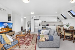 A modern living room with a sofa, TV, and dining area. - Comfortable 2 Bed Stay with Parking (Footscray)