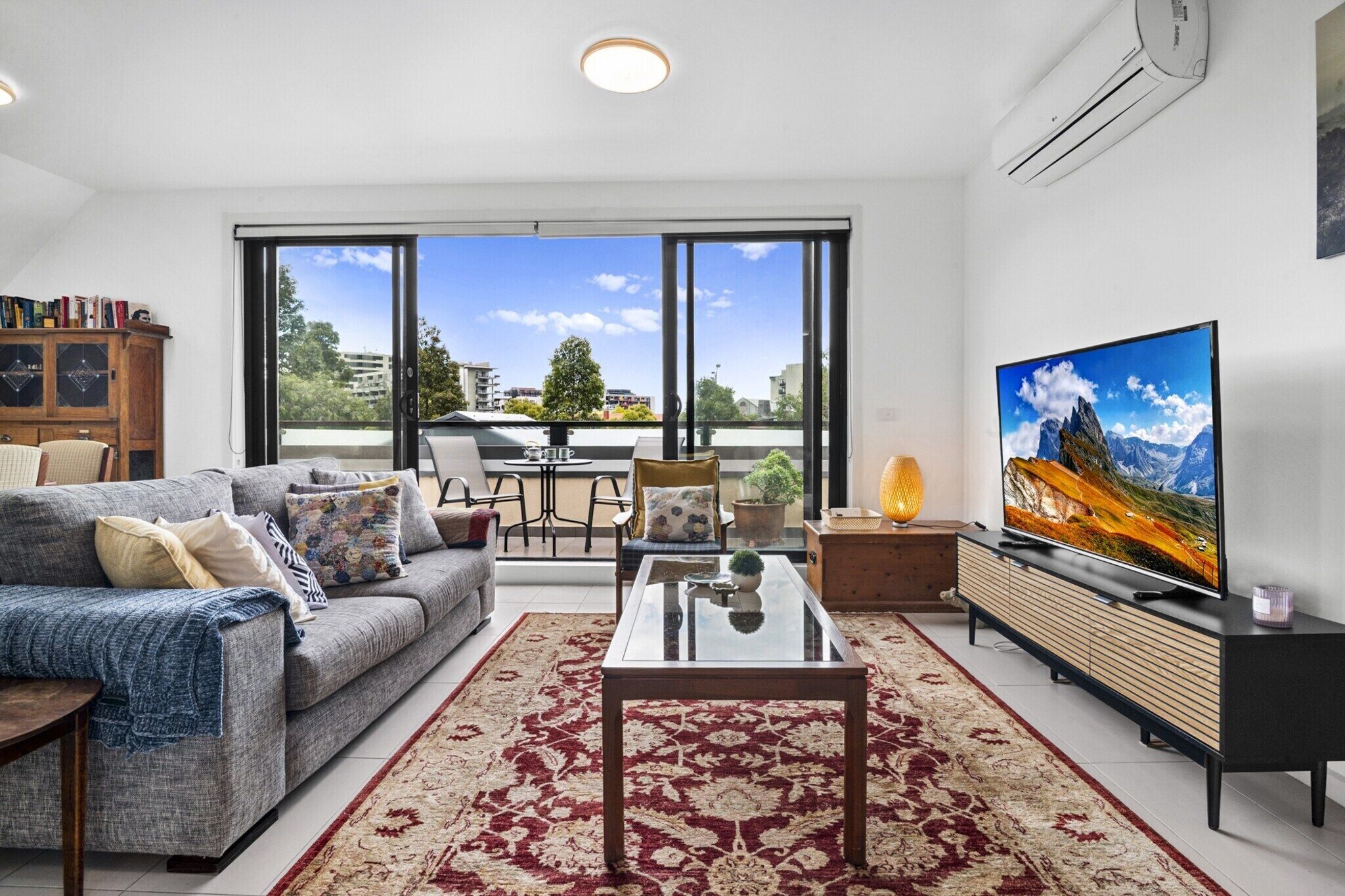 A modern living room with a sofa, coffee table, TV, and a large window offering a city view.