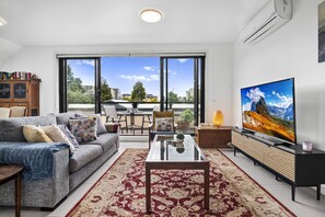Una sala de estar moderna con sofá, mesa de centro, televisor y un gran ventanal con vista a la ciudad.
