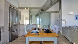 A modern kitchen with a dining table set for four, stainless steel appliances, and a grey sofa in the living area. - Finest Retreats | Gwynle (Criccieth)