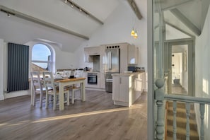 A modern kitchen with white cabinetry, a central island, and a dining area with a table and chairs. - Finest Retreats | Gwynle (Criccieth)