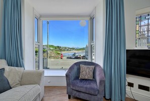 Een kamer met een bank, fauteuil en een groot raam met gordijnen.