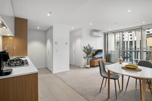 A modern kitchen with a stove, a dining area with a table and chairs, and a view of a cityscape through large windows. - Marina-View 1-Bed Apartment in Docklands (Docklands)