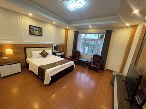 A hotel room with a bed, bedside tables, a desk, a chair, a TV, and a window with curtains. - G9 home Villa (Hanoi)
