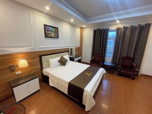 Habitación de hotel con cama, mesitas de noche, lámpara, una silla y ventana con cortinas.