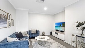 Ett modernt vardagsrum med en blå soffa, ett runt soffbord, en tv och en dekorativ spegel.