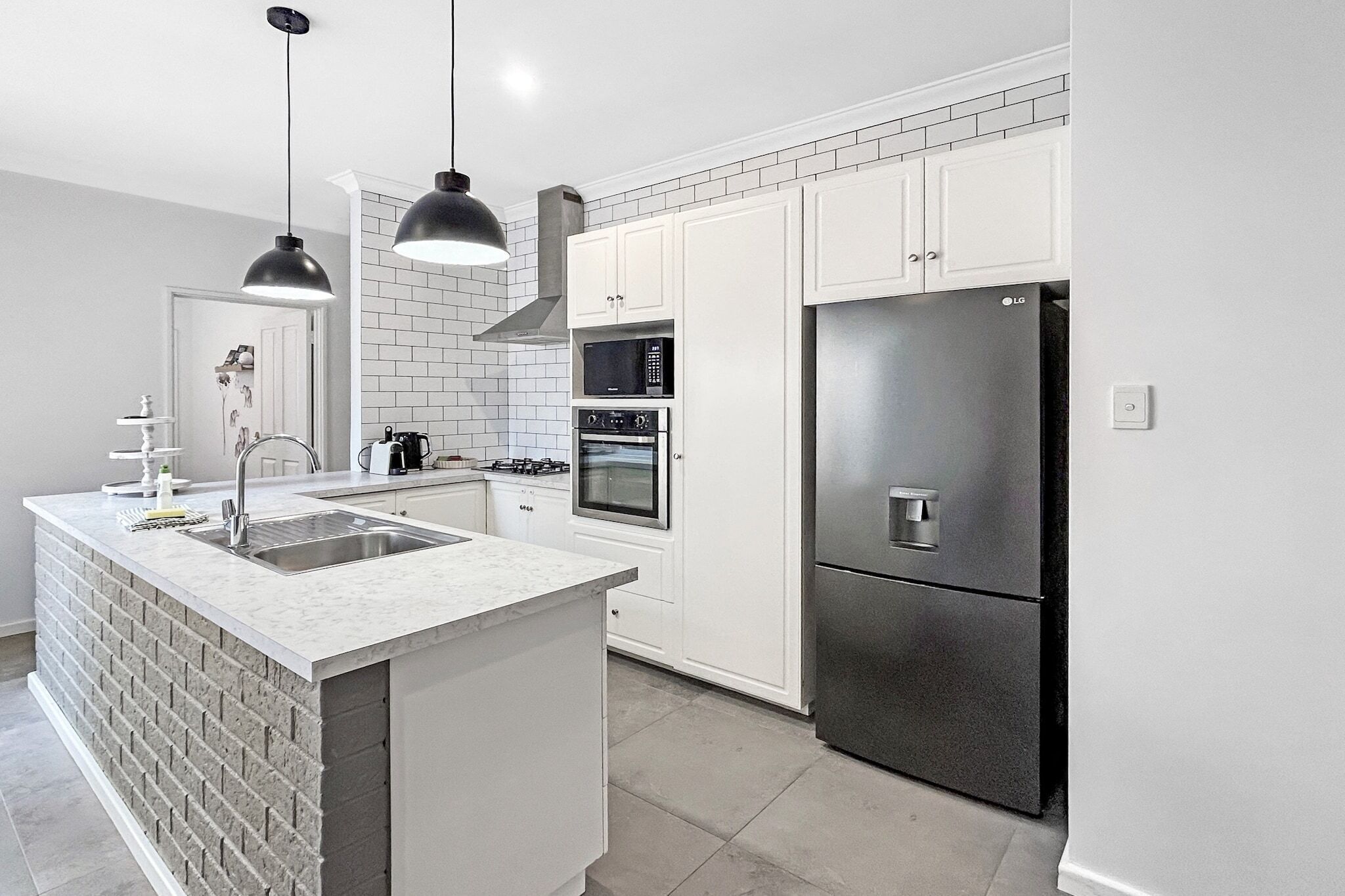 A modern kitchen with white cabinets, a stainless steel refrigerator, a built-in oven, and a marble island.