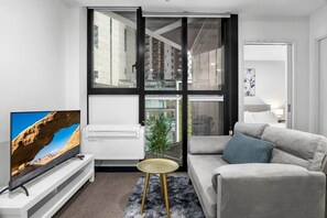 A modern living room with a flat-screen TV, a grey sofa, a small round table, and a large window with a city view. - Elevated 1-Bed Retreat Near Crown (Southbank)