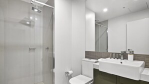 Un baño moderno con cabina de ducha de vidrio, inodoro y lavamanos con espejo.
