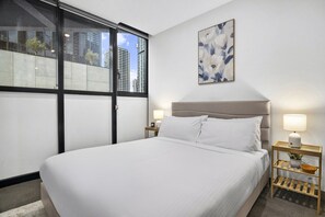 A hotel room with a large bed, two bedside tables with lamps, a window with a view of buildings, and a floral artwork on the wall. - Elevated 1-Bed Retreat Near Crown (Southbank)