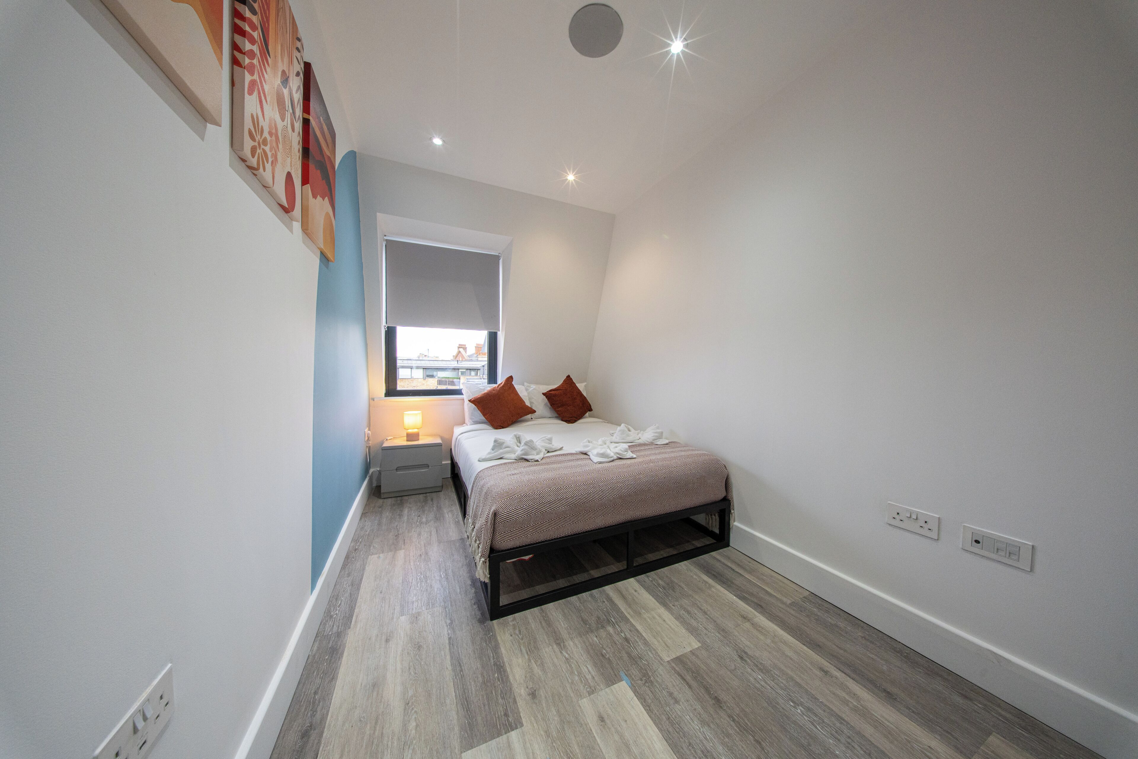 A bedroom with a bed, bedside table, wall-mounted light, and a window.