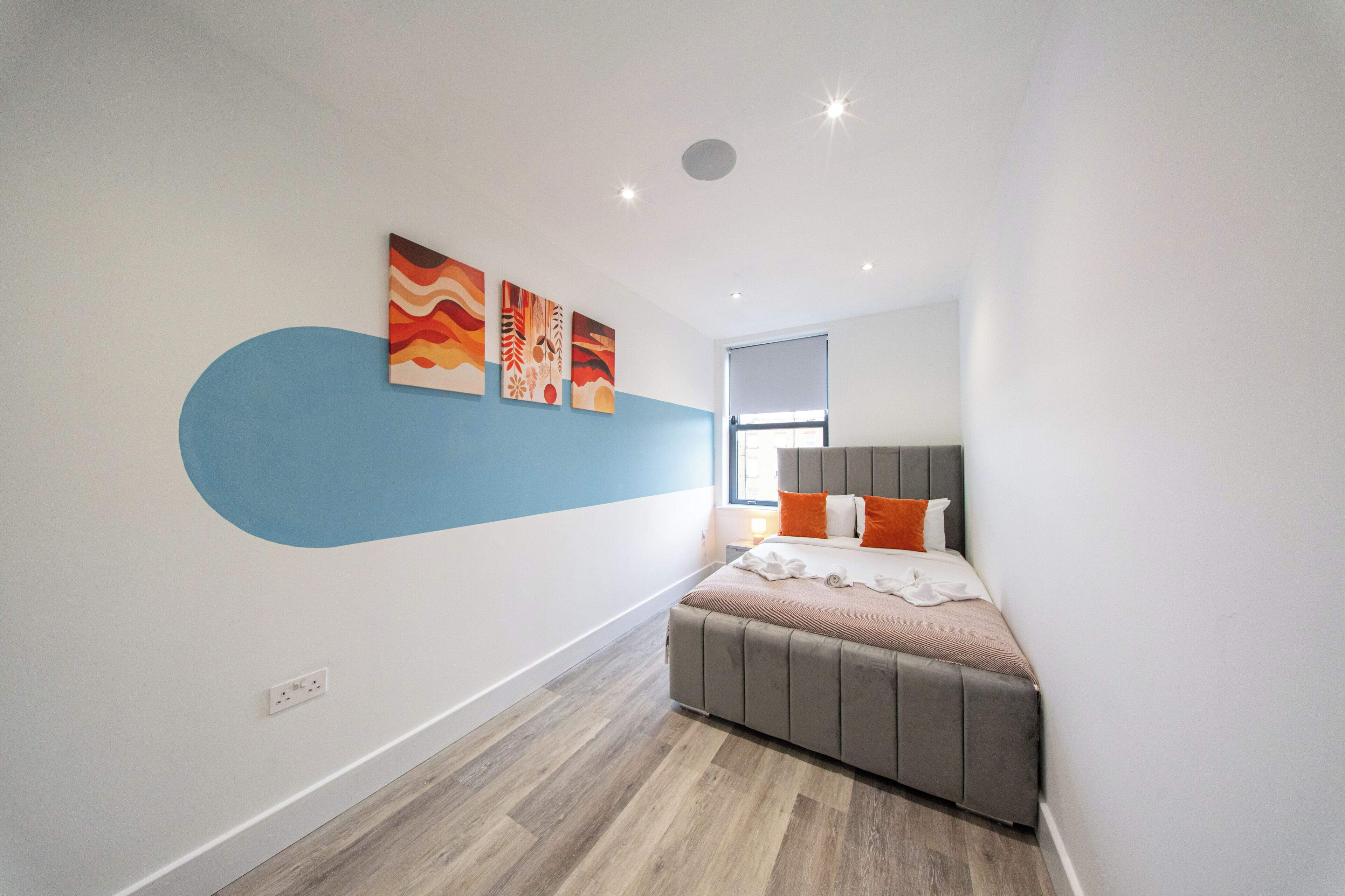 A modern bedroom with a bed, artwork on the wall, and a window.