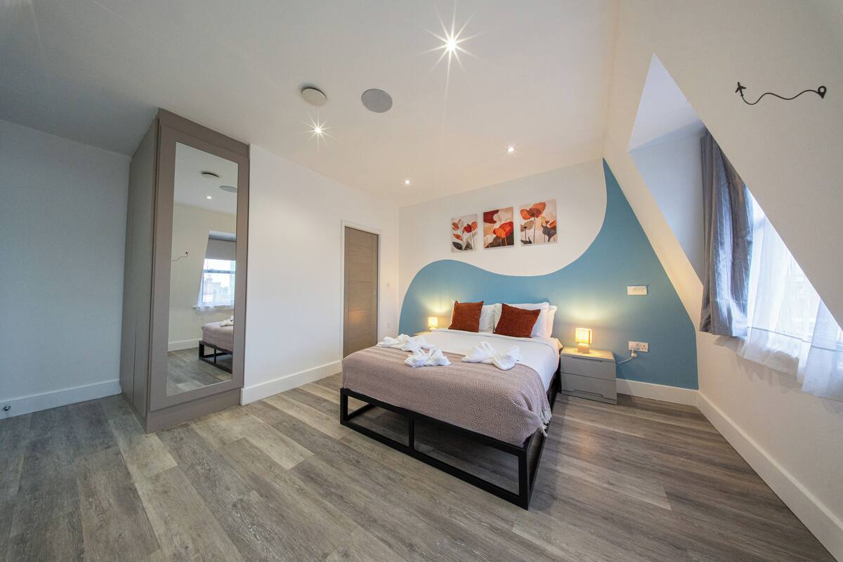 Quarto com cama, mesas de cabeceira, espelho e janela.