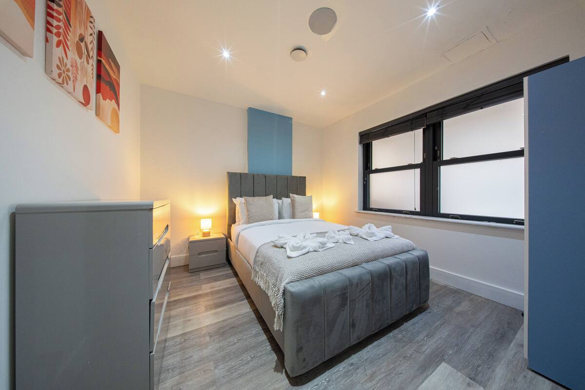 Quarto moderno com cama, mesas de cabeceira, guarda-roupa e janela.