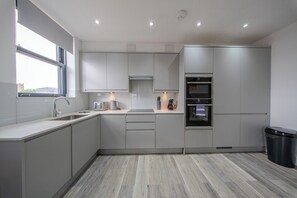 Een moderne keuken met grijze kastjes, een roestvrijstalen spoelbak, een ingebouwde oven en een raam voor natuurlijk licht.