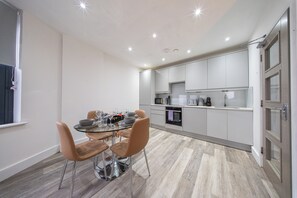 Een moderne keuken met witte kasten, een eettafel met stoelen en een inbouwoven.