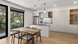 A modern kitchen with a dining area, large windows, and a view of trees. - Stylish 3-Bed Townhouse Near City Fringe (Everard Park)