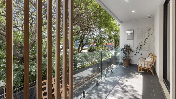 A balcony with a glass railing, potted plants, and wicker furniture. - Stylish 3-Bed Townhouse Near City Fringe (Everard Park)
