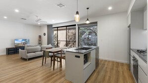 A modern kitchen with a central island, a dining area with a sofa and chairs, and a large window providing natural light. - Stylish 3-Bed Townhouse Near City Fringe (Everard Park)