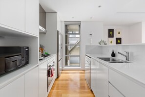 A modern kitchen with white cabinetry, stainless steel appliances, and a wooden floor. - Spacious 2-Bed Retreat in Rosebery (Rosebery)