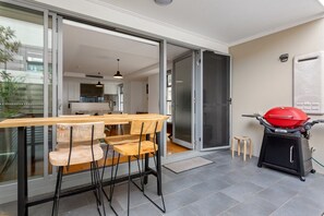 An open sliding glass door leading to a kitchen with a dining area, a barbecue grill, and a small stool. - Spacious 2-Bed Retreat in Rosebery (Rosebery)