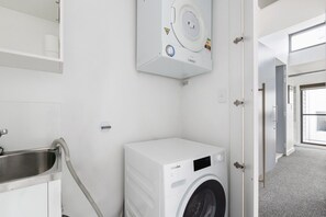 A laundry room with a washing machine, a sink, and a wall-mounted dryer. - Spacious 2-Bed Retreat in Rosebery (Rosebery)