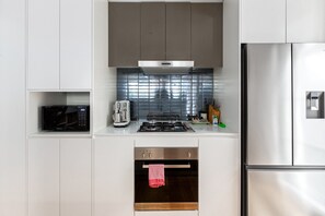 A modern kitchen with white cabinets, a stainless steel refrigerator, a microwave, a stove, and a toaster. - Spacious 2-Bed Retreat in Rosebery (Rosebery)