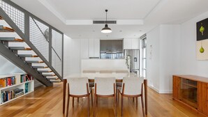 Een moderne keuken met een centraal eiland, een eetgedeelte met een lange tafel en stoelen, en een trap met een metalen leuning.