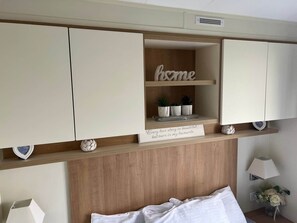 Un dormitorio con una cama, una estantería con plantas en macetas, un cartel con una cita y un letrero que dice 'hogar' en la pared.