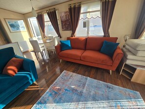 Un salon comprenant un canapé, un fauteuil bleu, une table à manger avec des chaises et un grand tapis.