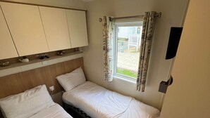 Een kamer met twee bedden, een televisie, een raam met gordijnen en een klein kastje.