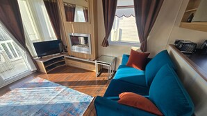 Een woonkamer met een blauwe bank, een flatscreentelevisie, een klein tafeltje en een raam met gordijnen.
