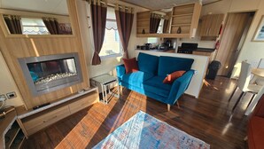Een ruimtelijk ingerichte leefruimte met kitchenette, een blauwe bank, een open haard en een groot vloerkleed.