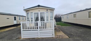 Une caravane avec une petite structure attenante, une porte blanche et une zone herbeuse en arrière-plan.