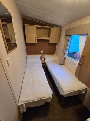 Une chambre compacte dans un camping-car, équipée de deux lits, d’un miroir et d’une fenêtre avec des rideaux.